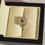Voici une bague en or blanc avec un diamant noir en son centre entouré de petits diamants blanc.